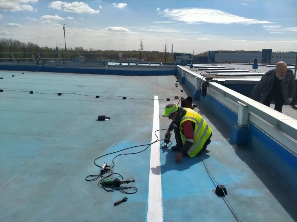 Кровельщик устанавливает ПВХ-мембрану на сварной шов плоской кровли