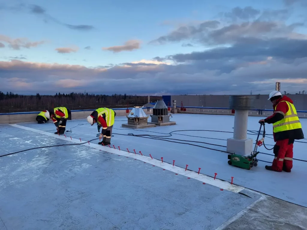 Монтаж ПВХ-мембраны в процессе: кровельщики выполняют сварку полотен на плоской кровле промышленного здания.