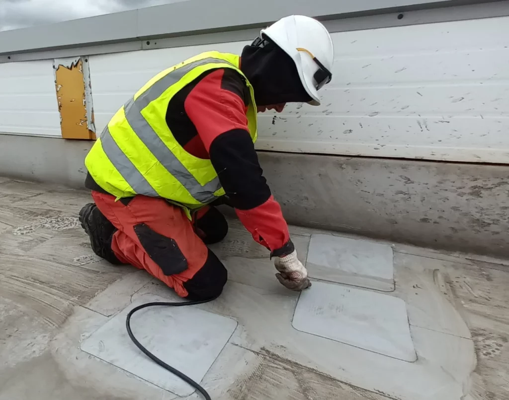 Кровельщик АНКОНС устанавливает заплатки на ПВХ–мембрану вдоль парапета на кровле завода Восход